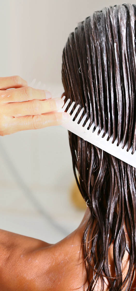 Ragazza mora, vista di spalle, in doccia, con i capelli bagnati e il fluido applicato. La ragazza di sta pettinando i capelli